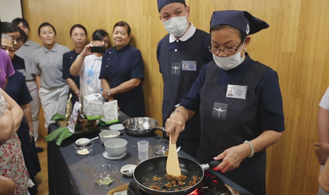 容敬坤師兄和黃錦梅師姊一邊烹調，一邊向民眾講解料理食材的步驟，還要立即回答民眾提出的問題，忙得不可開交，他們不辭勞苦的付出，便是慈悲。【攝影者：邢薇薇】